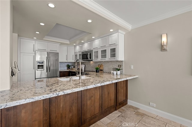 kitchen with light stone counters, stainless steel appliances, a peninsula, a sink, and tasteful backsplash