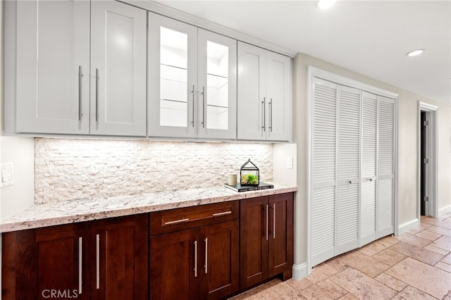 kitchen featuring recessed lighting, stone tile floors, baseboards, tasteful backsplash, and glass insert cabinets