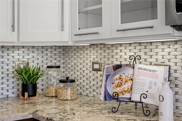 room details featuring glass insert cabinets, white cabinets, backsplash, and light stone countertops