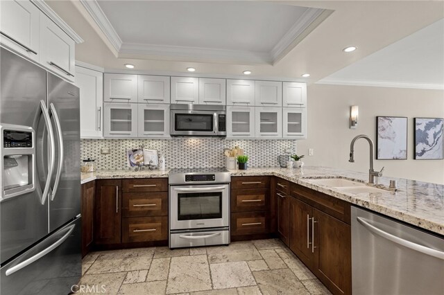 kitchen with stainless steel appliances, a tray ceiling, a sink, and stone tile flooring