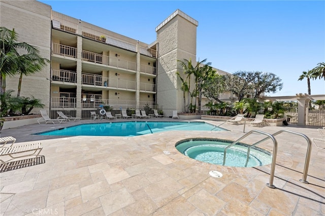 community pool with fence, a hot tub, and a patio