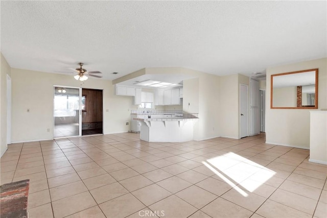 unfurnished living room with a ceiling fan, a textured ceiling, baseboards, and light tile patterned floors