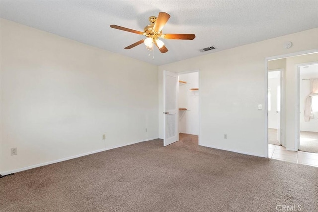 unfurnished bedroom with a textured ceiling, light colored carpet, a ceiling fan, visible vents, and a walk in closet