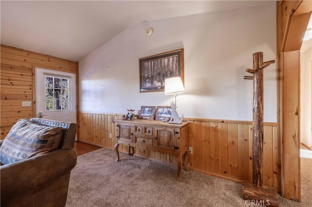 living area featuring lofted ceiling, a wainscoted wall, wood walls, and carpet