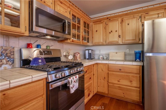 kitchen with stainless steel appliances, tile counters, decorative backsplash, and wood finished floors