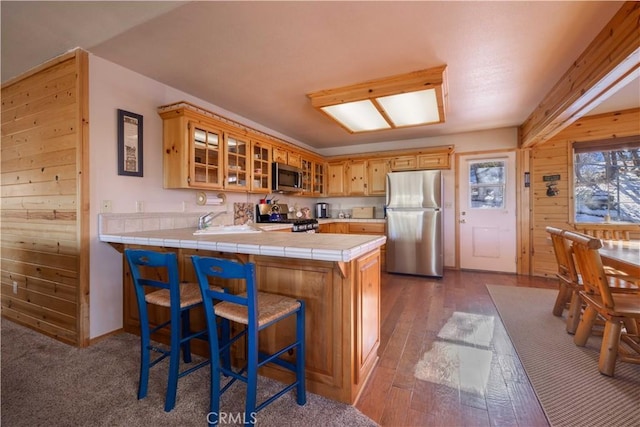 kitchen with stainless steel appliances, tile counters, glass insert cabinets, a sink, and a peninsula