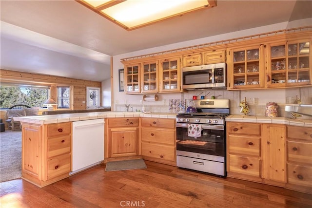 kitchen with a peninsula, appliances with stainless steel finishes, dark wood finished floors, and tile counters