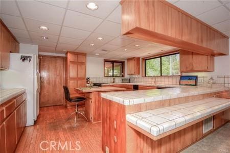 kitchen with a drop ceiling, a peninsula, light wood-type flooring, freestanding refrigerator, and tasteful backsplash