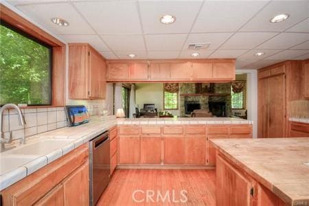 kitchen with visible vents, backsplash, light wood-style flooring, stainless steel dishwasher, and a sink