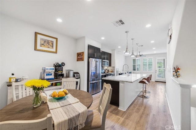 kitchen with a center island with sink, visible vents, appliances with stainless steel finishes, a sink, and light wood-type flooring