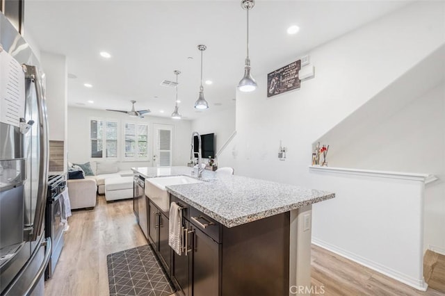 kitchen featuring open floor plan, appliances with stainless steel finishes, light wood finished floors, and dark brown cabinetry