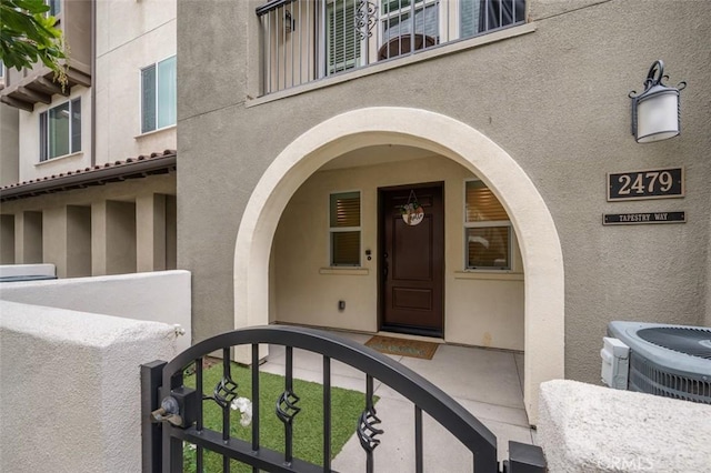 view of exterior entry featuring a gate, central AC unit, and stucco siding