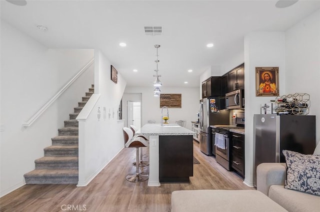 kitchen with a kitchen breakfast bar, stainless steel appliances, visible vents, and light wood-style floors