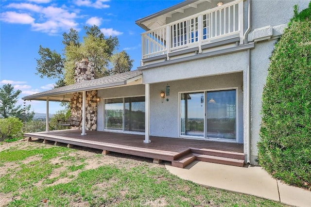 rear view of property with a balcony, a chimney, and stucco siding