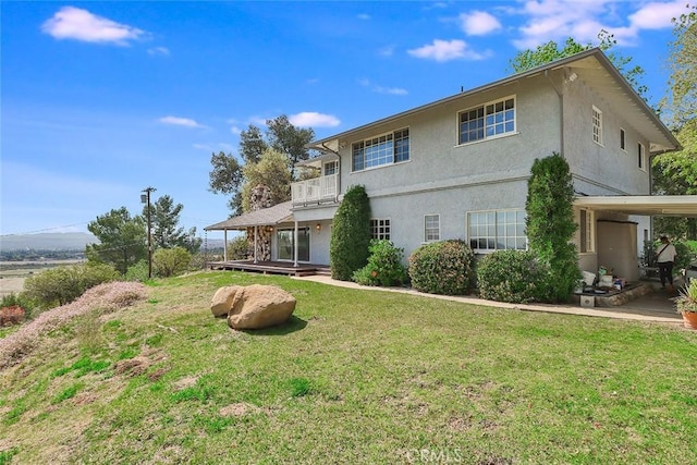 rear view of house featuring a balcony, a lawn, and stucco siding