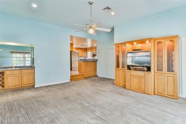 unfurnished living room with visible vents, ceiling fan, beverage cooler, light colored carpet, and a sink