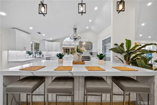 kitchen with white cabinets, premium appliances, lofted ceiling, hanging light fixtures, and a sink