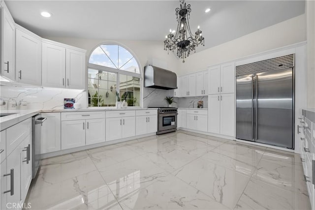 kitchen with white cabinetry, high quality appliances, marble finish floor, wall chimney range hood, and tasteful backsplash