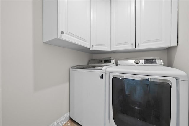 clothes washing area with washing machine and dryer, cabinet space, and baseboards