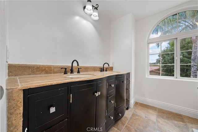 bathroom featuring stone finish floor, a sink, baseboards, and double vanity