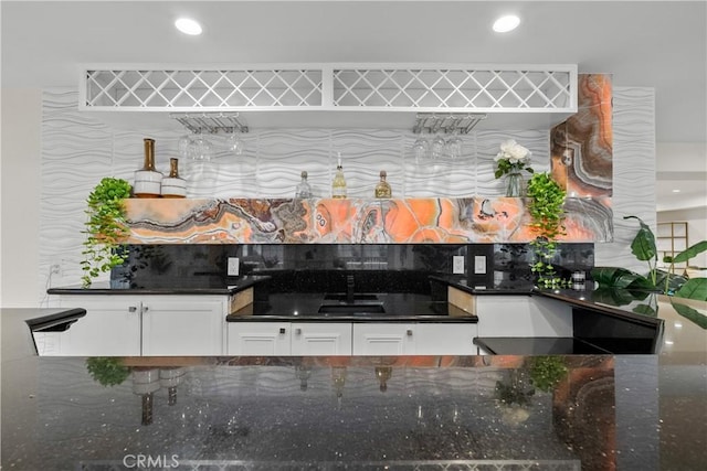 kitchen with tasteful backsplash, dark stone countertops, white cabinetry, a sink, and recessed lighting