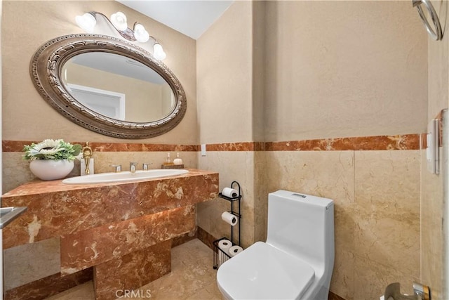 half bath featuring a sink, a wainscoted wall, toilet, and tile walls