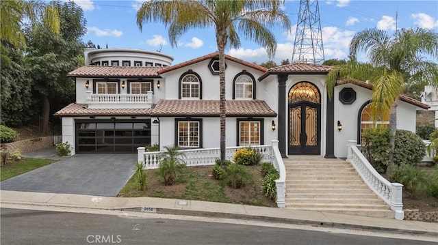 mediterranean / spanish-style house featuring a garage, concrete driveway, a balcony, a tiled roof, and stucco siding