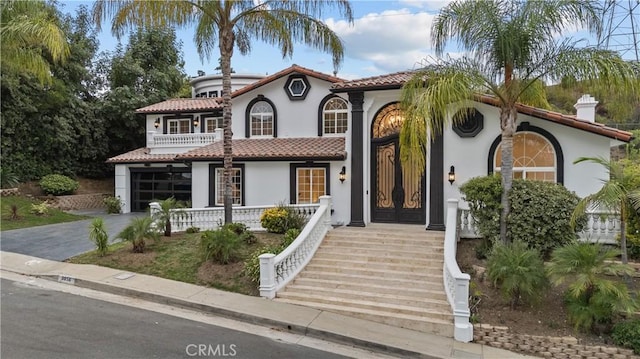 mediterranean / spanish home with a balcony, a garage, a tile roof, driveway, and stucco siding