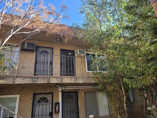 multi unit property with a wall mounted AC, a balcony, and stucco siding