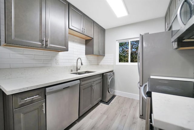 kitchen with backsplash, appliances with stainless steel finishes, light wood-style floors, a sink, and washer / dryer