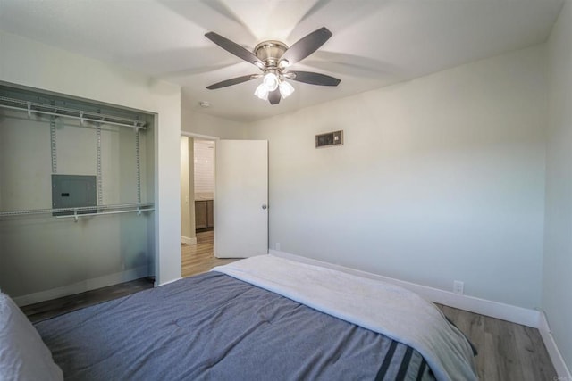 bedroom featuring a closet, ceiling fan, wood finished floors, electric panel, and baseboards