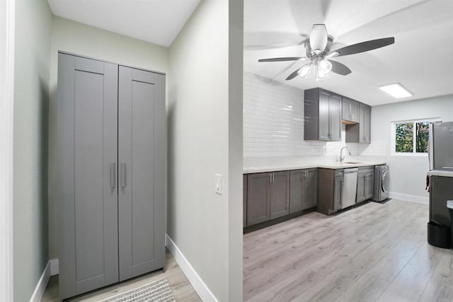 kitchen with appliances with stainless steel finishes, a sink, light countertops, light wood-type flooring, and backsplash