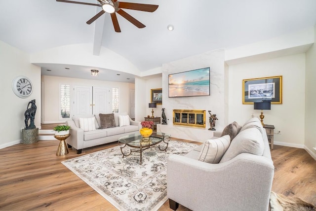 living area with a ceiling fan, baseboards, vaulted ceiling with beams, a high end fireplace, and light wood-type flooring