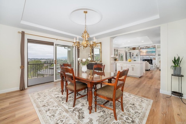 dining area with a tray ceiling, baseboards, light wood-style floors, and a notable chandelier