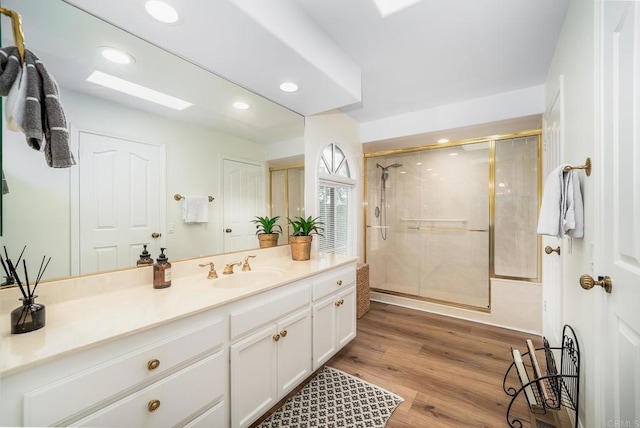 full bathroom with wood finished floors, recessed lighting, a skylight, a shower stall, and vanity