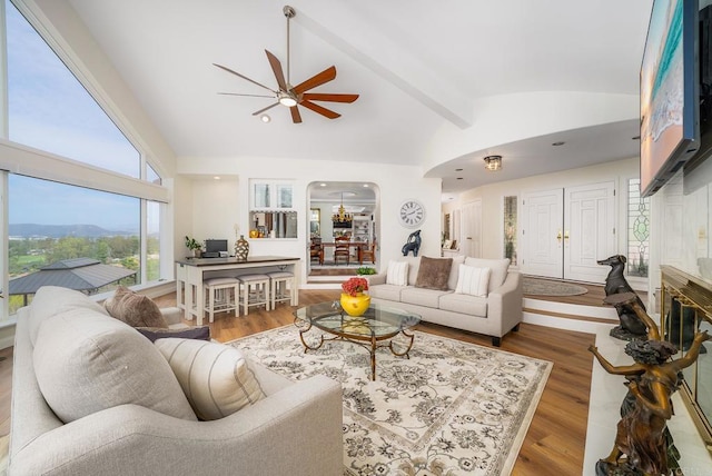 living area featuring arched walkways, lofted ceiling with beams, a ceiling fan, and wood finished floors