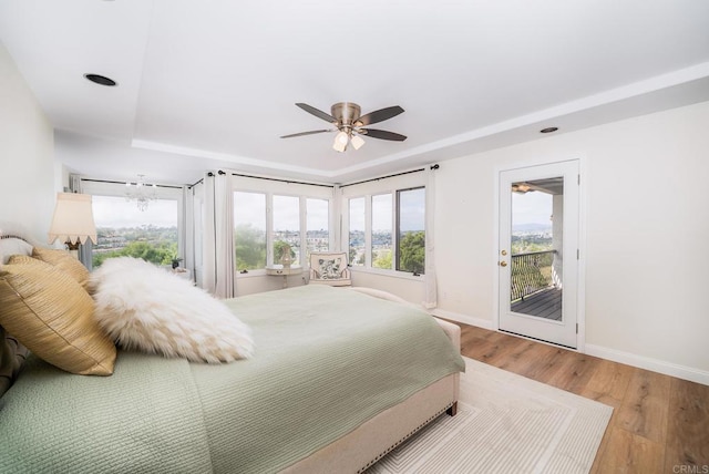 bedroom with ceiling fan, baseboards, wood finished floors, a raised ceiling, and access to outside