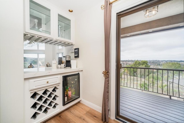 bar featuring light wood-type flooring, wine cooler, baseboards, and a dry bar