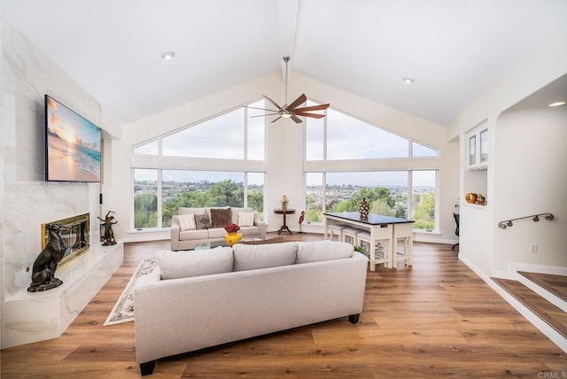 living area featuring a premium fireplace, wood-type flooring, high vaulted ceiling, and ceiling fan