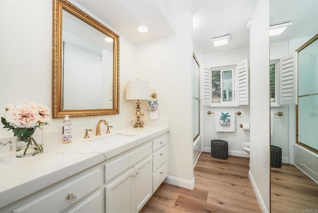 bathroom featuring vanity, toilet, wood finished floors, and enclosed tub / shower combo