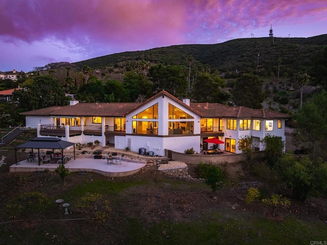 back of property at dusk featuring a patio area, central air condition unit, a mountain view, and a chimney