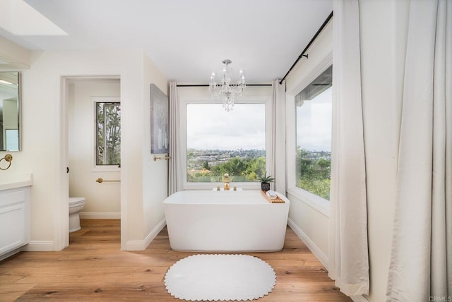 bathroom featuring a freestanding bath, toilet, an inviting chandelier, wood finished floors, and vanity