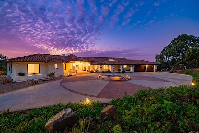 view of front of property featuring a patio area, curved driveway, stucco siding, and a tiled roof