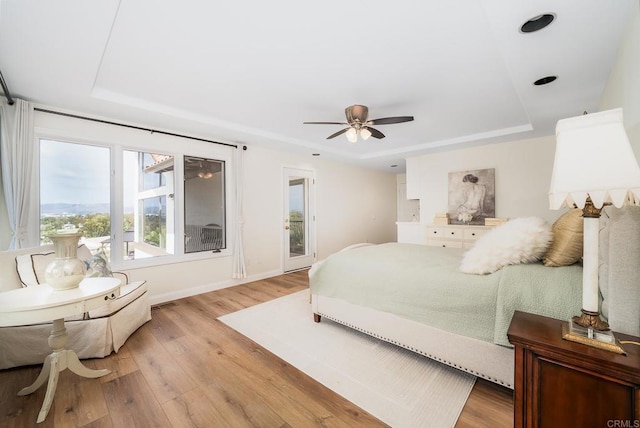 bedroom with a tray ceiling, baseboards, and light wood-style flooring