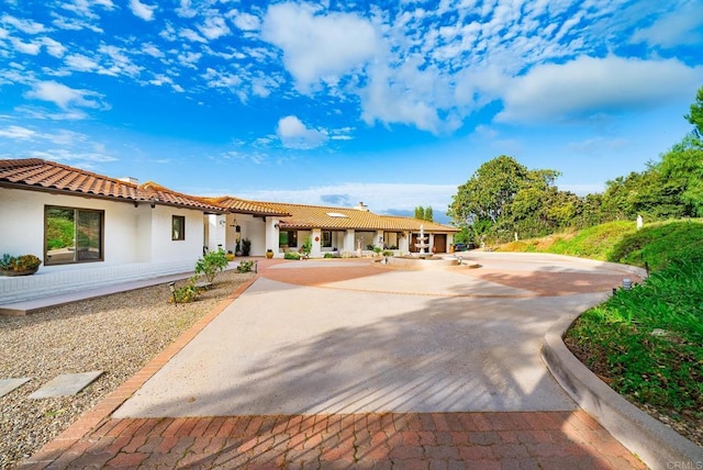 view of front facade with a tile roof, driveway, and stucco siding