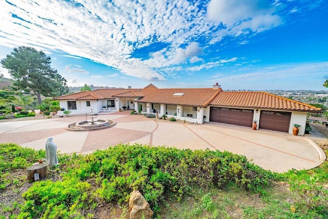 view of front of property featuring concrete driveway, a tiled roof, a garage, and a chimney