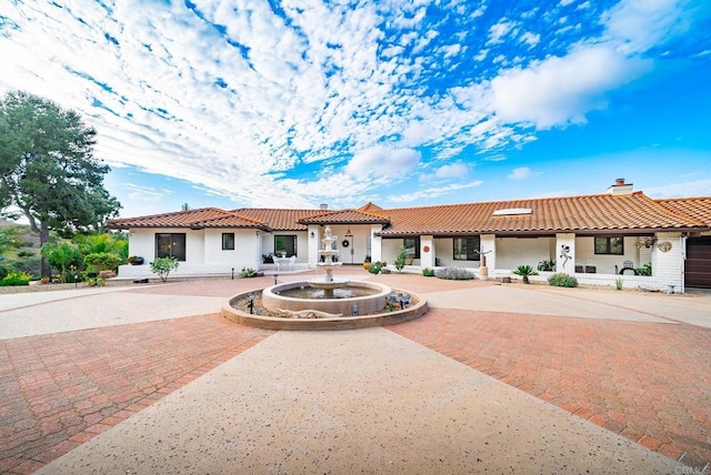 mediterranean / spanish-style house with curved driveway, a tiled roof, a chimney, and stucco siding