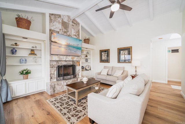 living room featuring beamed ceiling, arched walkways, light wood-style floors, and a fireplace