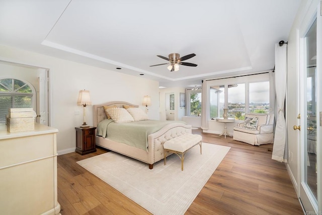 bedroom with a tray ceiling, multiple windows, and wood finished floors