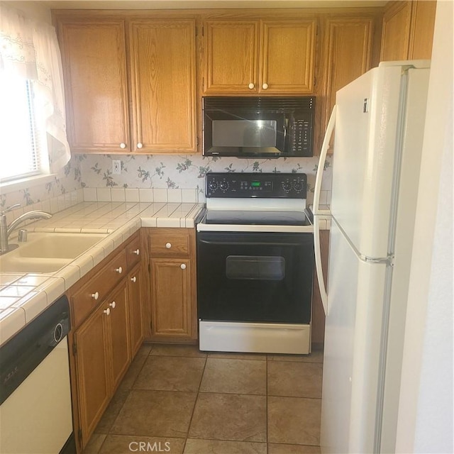 kitchen with white appliances, tile counters, brown cabinetry, a sink, and light tile patterned flooring